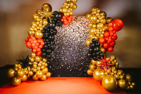 Dekorative Ballonwand in Schwarz, Gold und Rot mit glitzerndem Hintergrund.